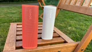 Sonos Roam in white behind Sonos Roam 2 in orange red on garden chair