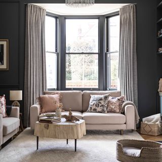 living room colour mistakes, living room with charcoal grey walls and woodwork, blush furniture, wooden coffee table, cream rug, patterned cushions, pale grey curtains