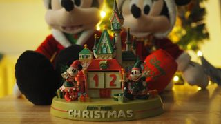 Disney Christmas Countdown Castle in front of a Mickey and Minnie Mouse plush set, with a twinkling tree in the background