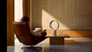 A woman sitting in a chair next to the Dyson Cool CF1 bladeless fan