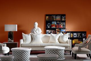 A living room with a white sofa and walls painted a rich burnt orange colour