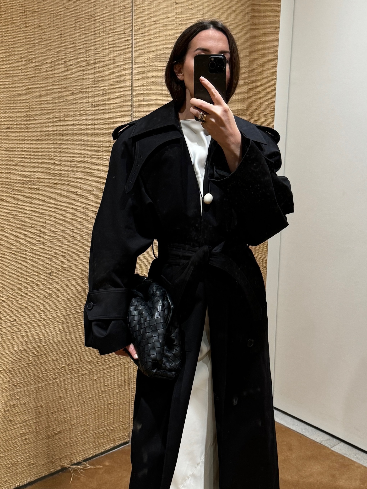 Caitlin Burke wearing a white dress and black coat and carrying a Bottega Veneta Pouch.