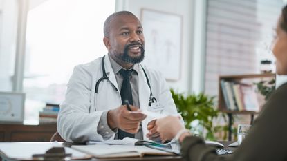 A doctor smiles as he hands a patient a prescription.