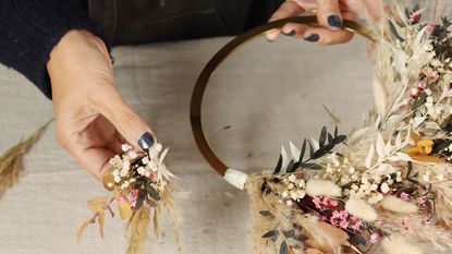 Hands adding small bunches of dried flowers and pampas grass to a wreath