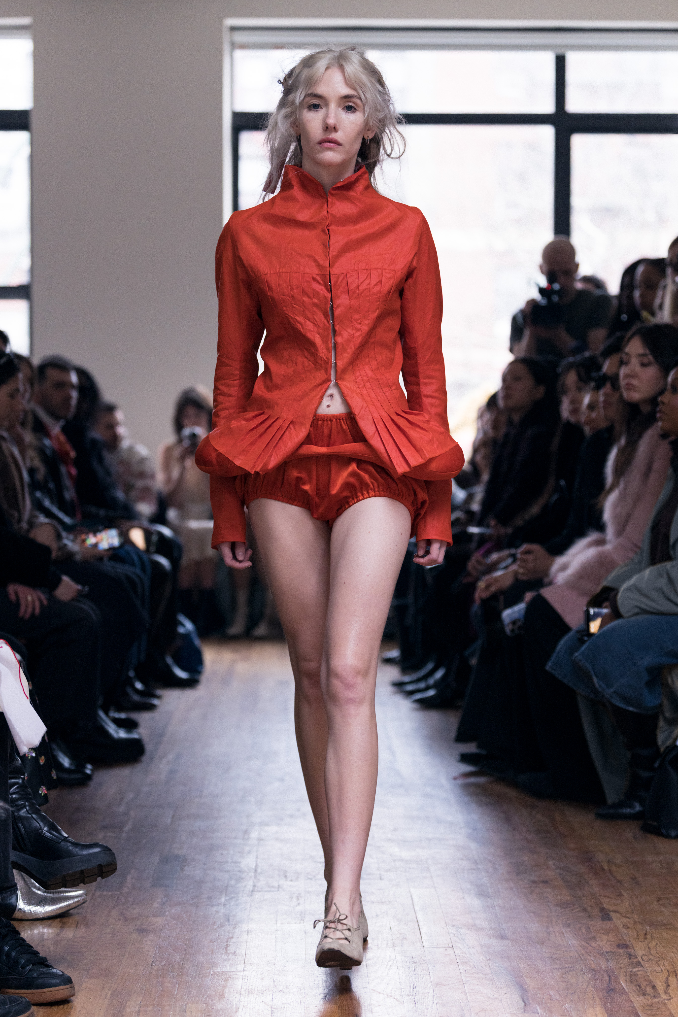 A model wearing a red-orange persimmon colored jacket and satin shorts on Zoe Gustavia Anna Whalen Fall 2026's runway