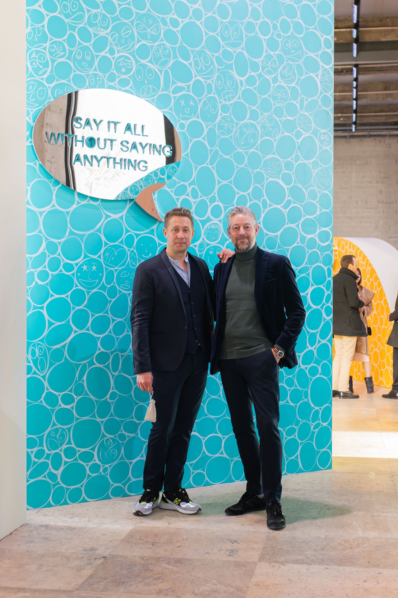 Jeppe Hein and Adam Byatt in front of Jeppe Hein artwork with a speech bubble mirror that says &quot;Say it all without saying anything&quot;. 