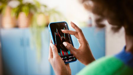 Woman holding a phone and zooming in on an image of stock charts 