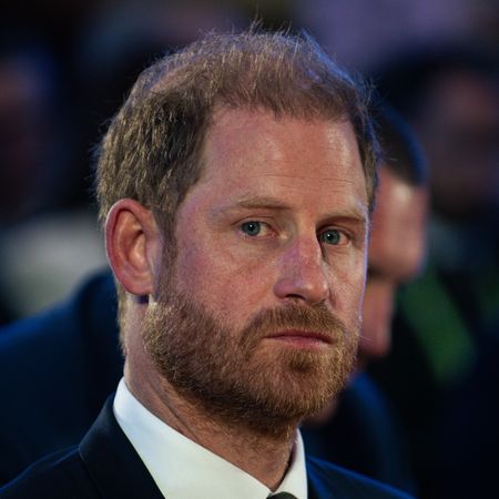 Prince Harry has red hair and looks seriously at the camera while wearing a navy suit and white shirt in 2026