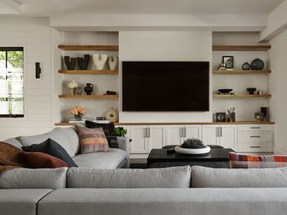 living room with gray sectional sofa and alcove shelving with TV between and white walls