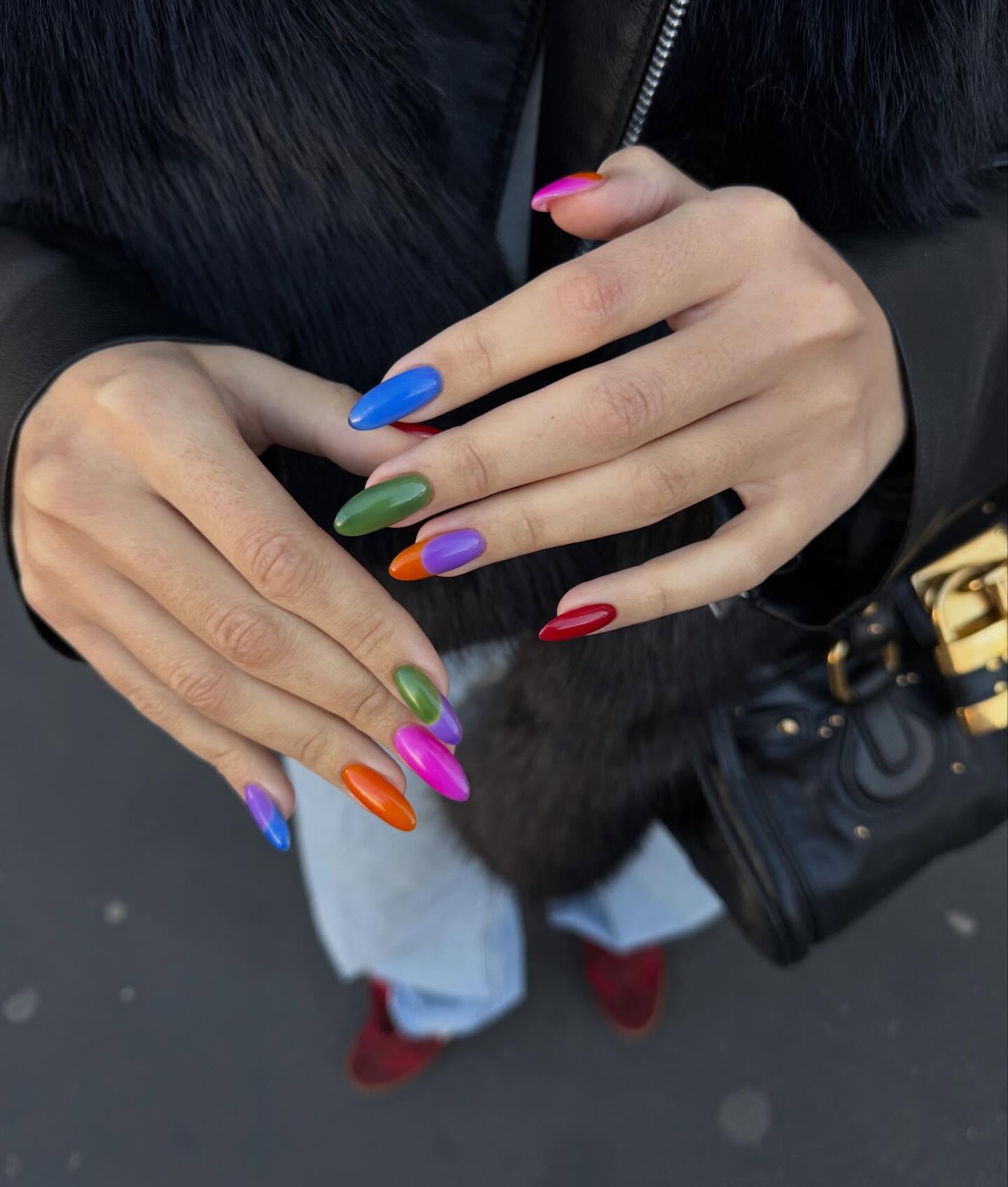 a woman with a fur coat, jeans, black bag, and red shoes with long almond nails featuring an array of nail polish colors