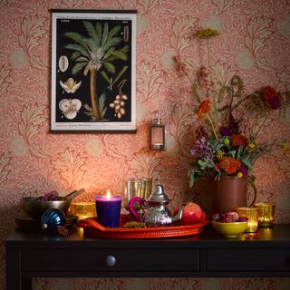 Wooden table topped with flowers, candles and tea with a floral wallpaper background