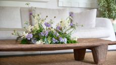 A low-slung wood table with a purple and white floral centerpiece in a living room