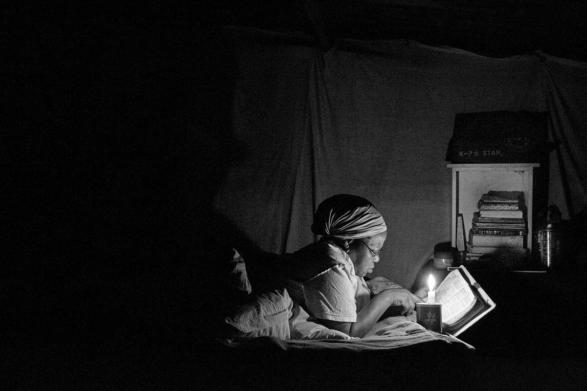 Black and white photograph of a woman lying on her stomach reading a bible by candlelight