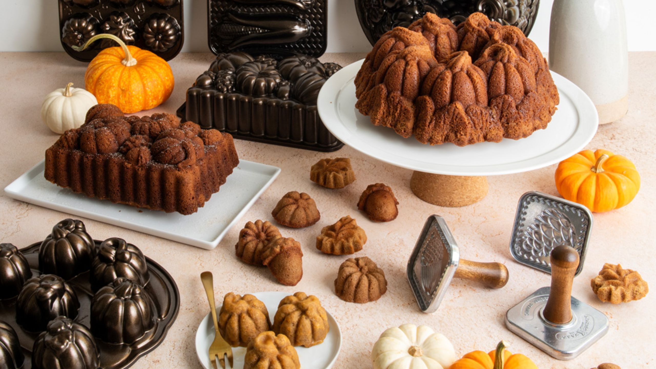 A selection of NordicWare Fall Bakeware surrounded by cakes. 