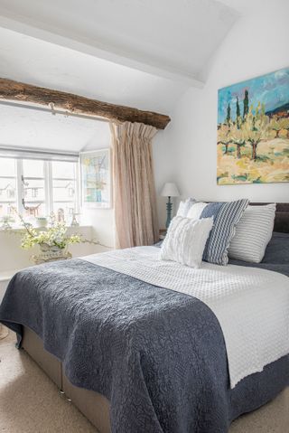 bedroom with double bed and grey bed throw with bright painting at bedhead and beam over dormer window
