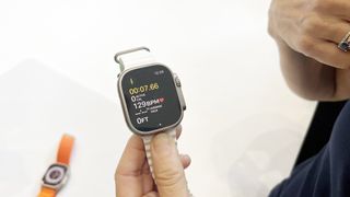 En hand som håller upp en Apple Watch Ultra med ett vitt armband.