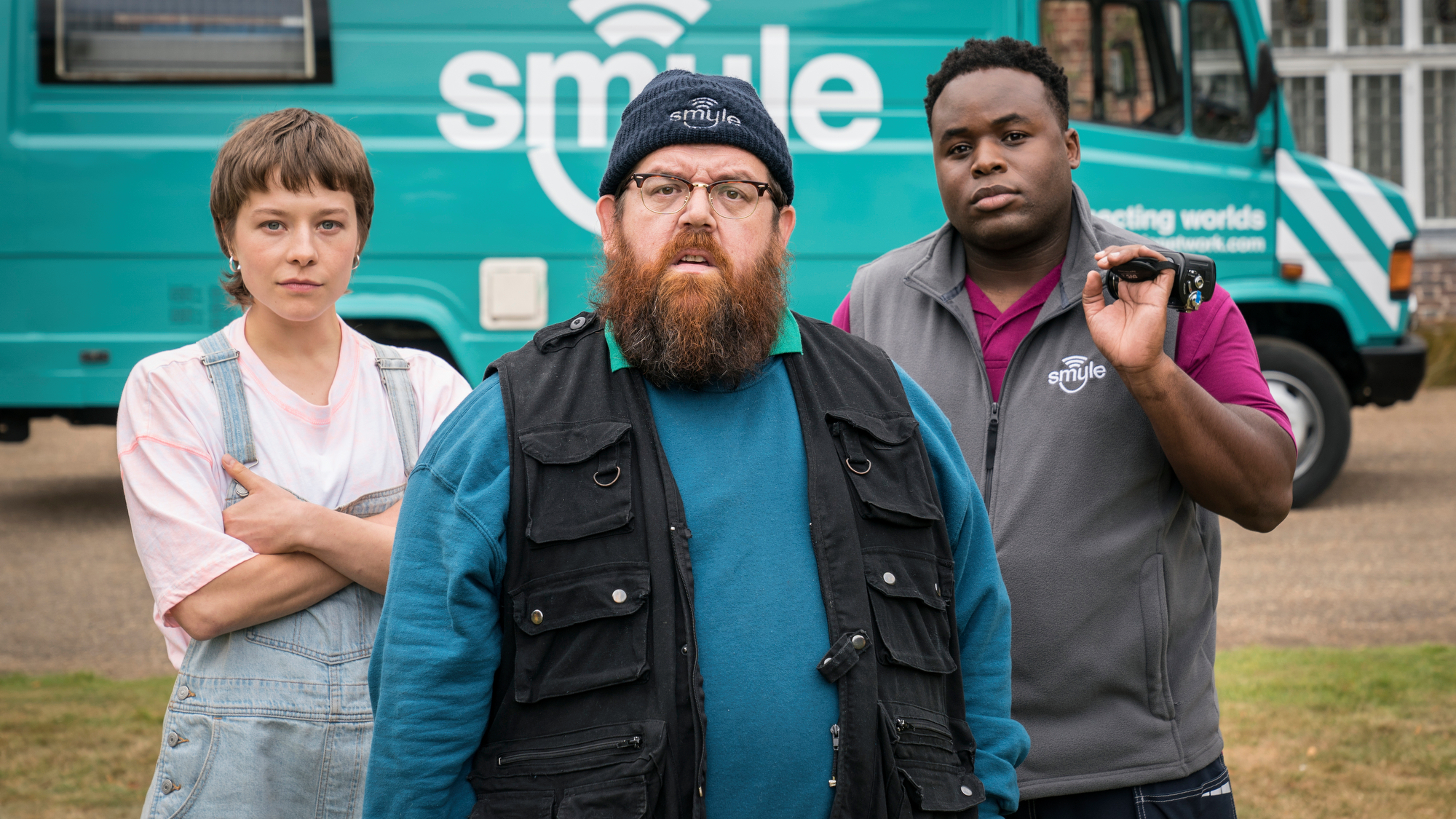 L-R: Astrid (Emma D'Arcy), Gus (Nick Frost) and Elton (Samson Kayo) stand in front of a Smyle van for Prime Video's "Truth Seekers"