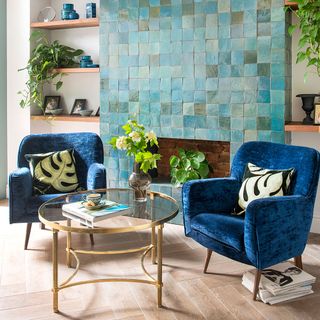 A tiled teal feature wall above a fireplace in a living room with two blue armchairs