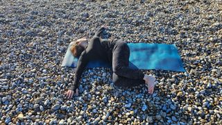 Jennifer performing a supine twist on yoga mat at the beach