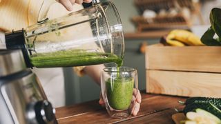 a photo of someone poring a green smoothie into a glass from a blender