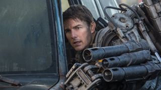 Tom Cruise as Major William Cage holding a massive gun during the sci-fi movie Edge of Tomorrow.