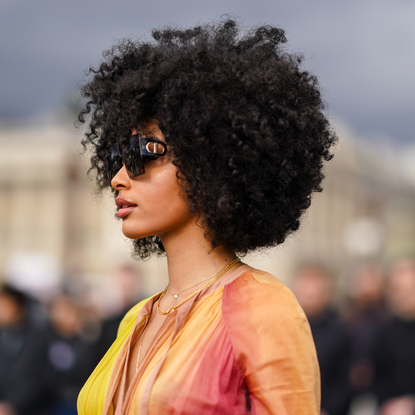 A guest wears Dior sunglasss, a yellow and pink pleated dress, outside Dior, during Paris Fashion Week - Womenswear Fall/Winter 2020/2021, on February 25, 2020 in Paris, France.