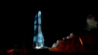 a large white rocket stands upright on a launch pad while a huge cloud of smoke erupts from beneath it