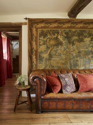 leather chesterfield sofa with red cushions in front of a tapestry