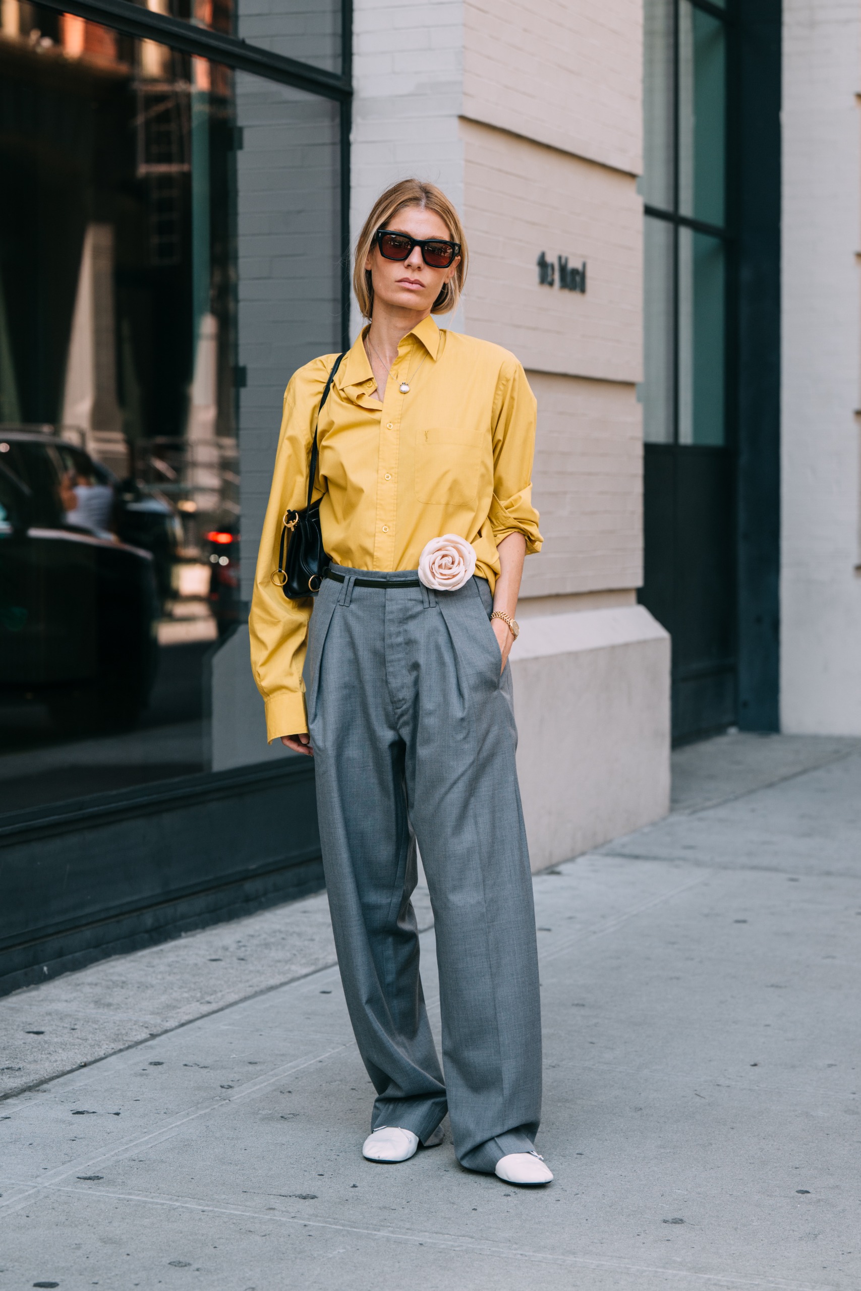 woman wearing a yellow button down shirt gray trousers and a floral corsage on belt