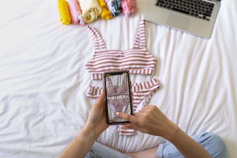 Person taking smartphone picture of bikini on bed