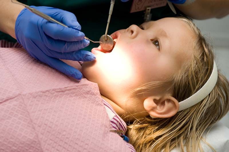 Adorable little blond girl getting her teeth checked at the dentist 