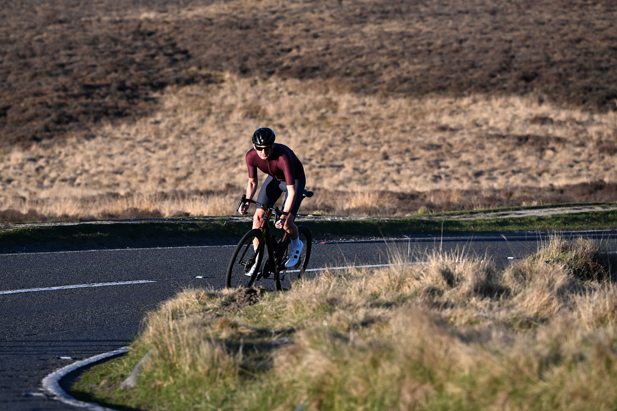 Man wearing a burgundy jersey riding out of the saddle on a Handsling bike round a corner on a moorland road