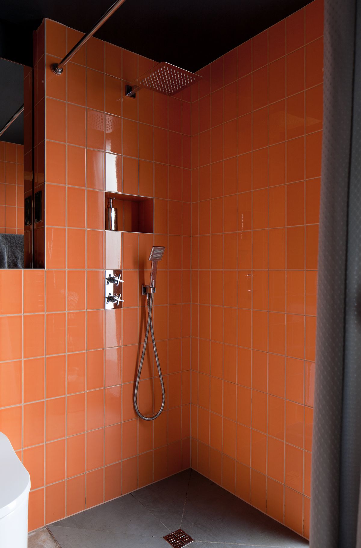 A bathroom shower with orange tiles and black walls
