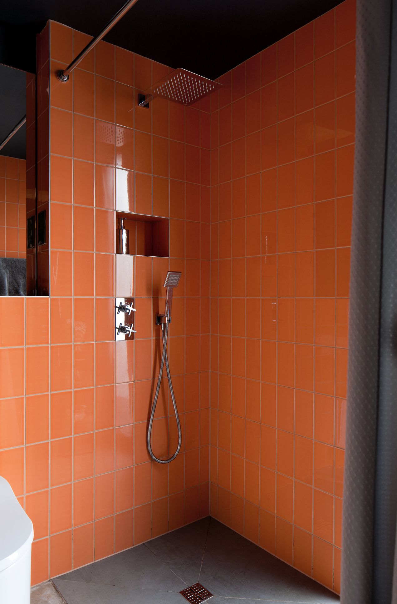 A bathroom shower with orange tiles and black walls
