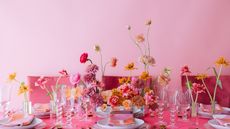 Vibrant pink tablescape with lots of pink, peach and orange flowers in vases, pink table cloth and pink background wall