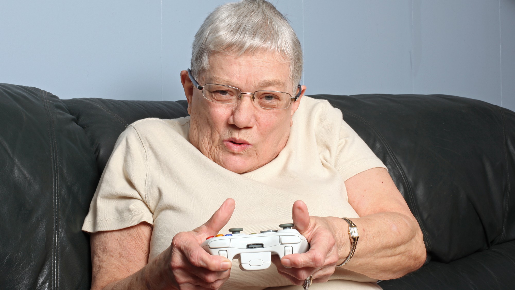 An older woman holds a video game controller and is engrossed in a game.