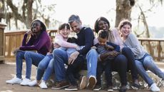 A blended family smile and laugh as they jockey for position on a bench in a park.