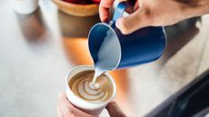 A barista pouring steamed milk into a cup, making latte art