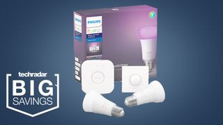 The Philips Hue White and Colour Ambiance starter kit components of two bayonet fitting bulbs, a Hue Bridge, and Hue button on a blue background