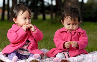 Twin girls sit in a park eating.