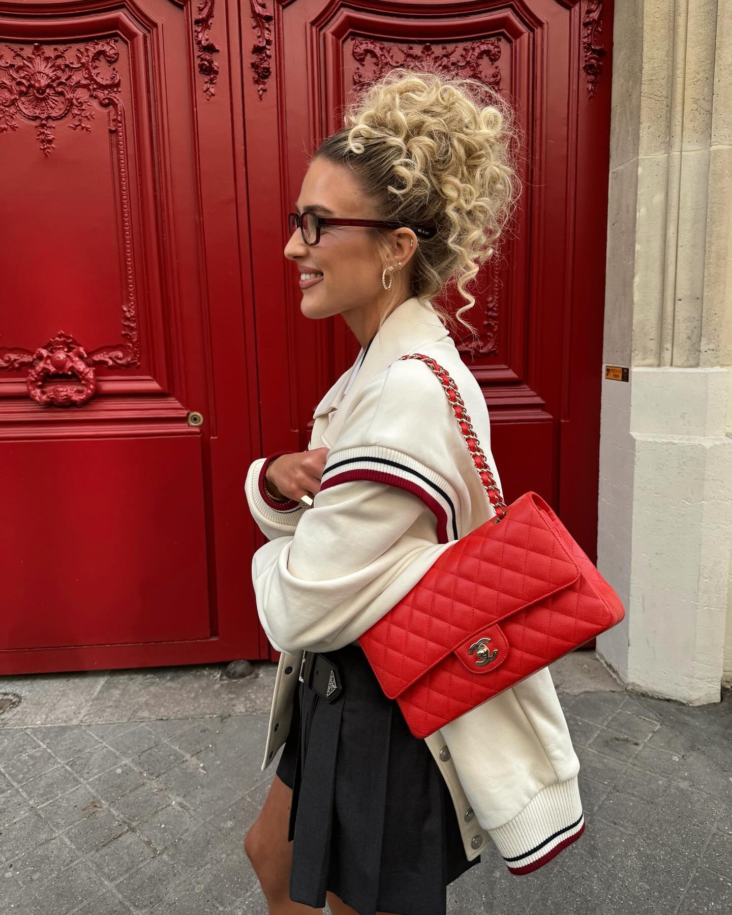 A woman wearing a red bag, white longsleeve shirt and black pleated skirt