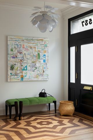 A light entryway with brightly colored piece of art and green chaise lounge.