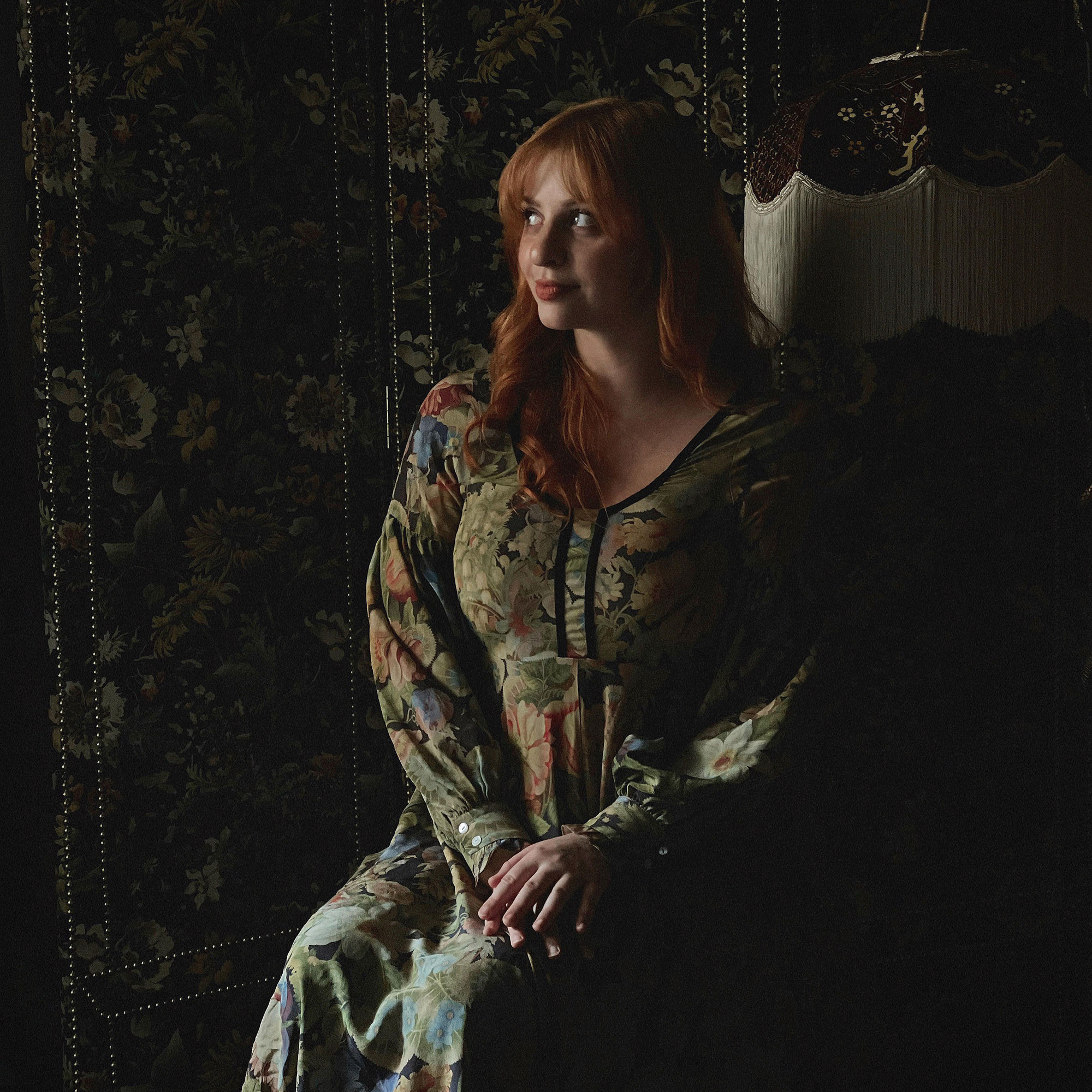 White woman with red hair in long floral dress in dark floral room is Maggie Samson from House of Hackney