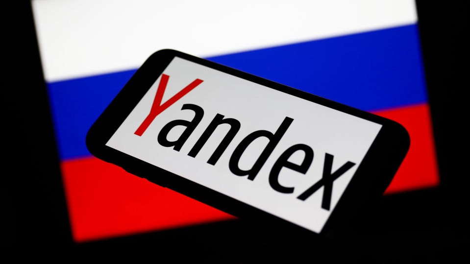 Yandex logo displayed on a phone screen and Russian flag displayed on a screen in the background