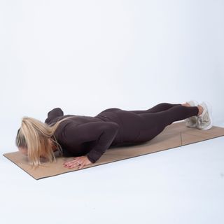 woman wearing black workout clothes performing a pushup on an exercise mat against a white background.