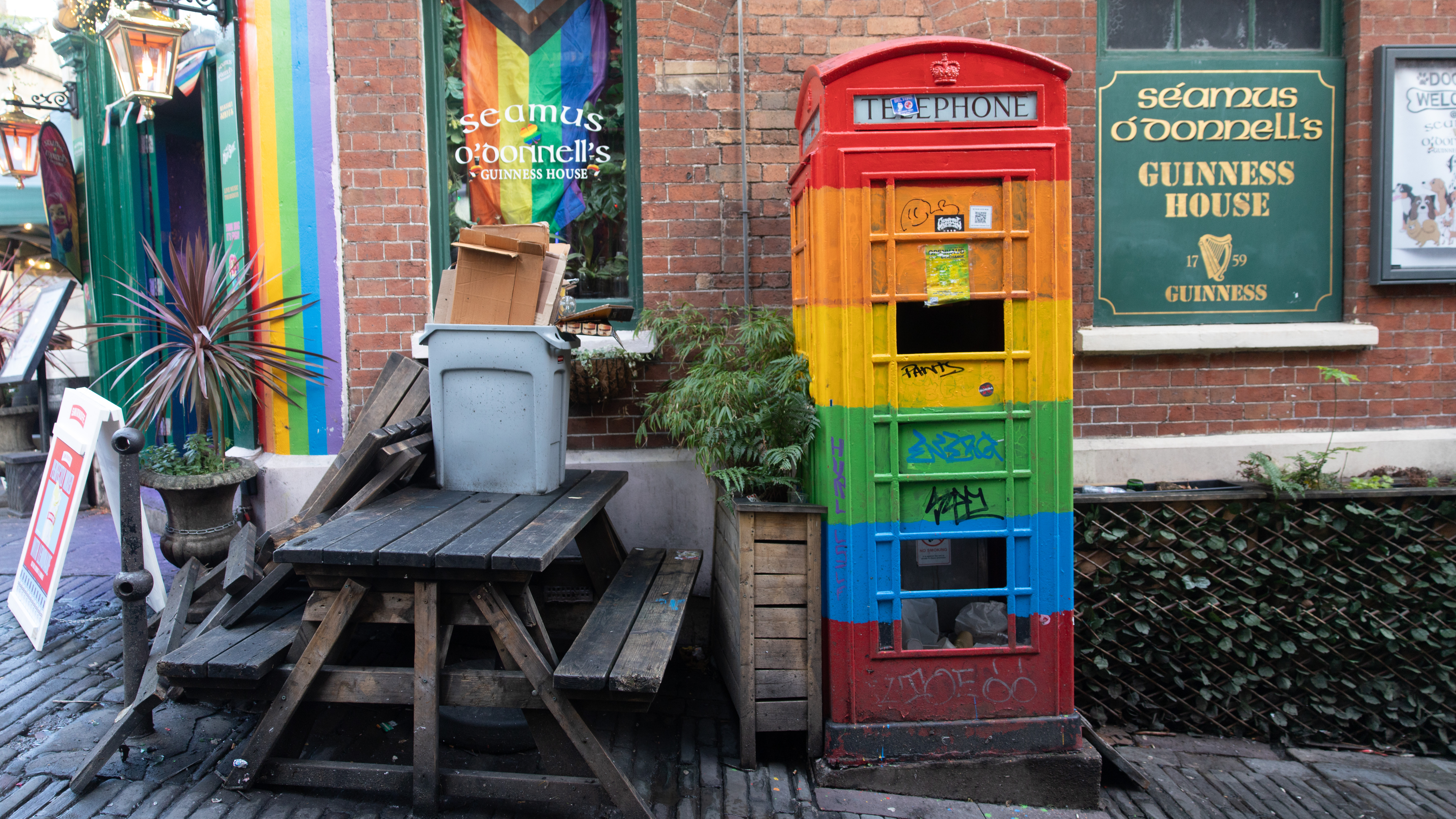 Outside shot of a pub in Bristol, with a bench and multi-coloured phone box painted in rainbow colours.