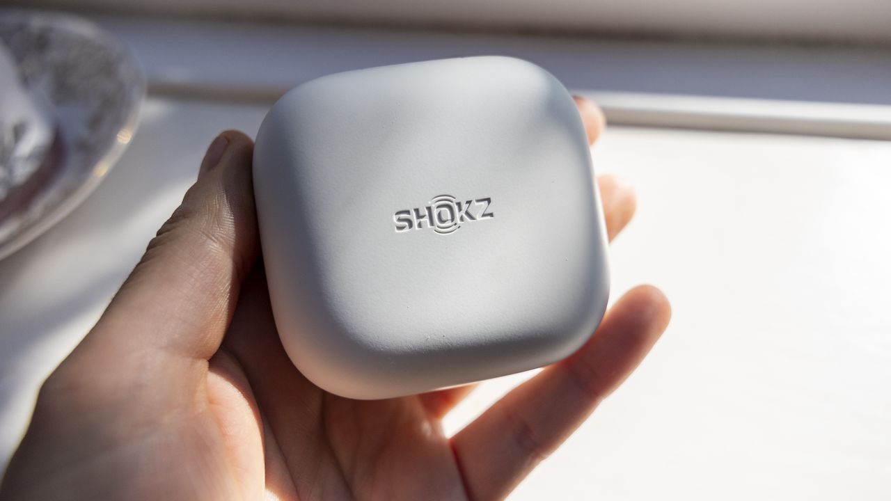 The Shokz OpenFit Air headphone case held in a female hand