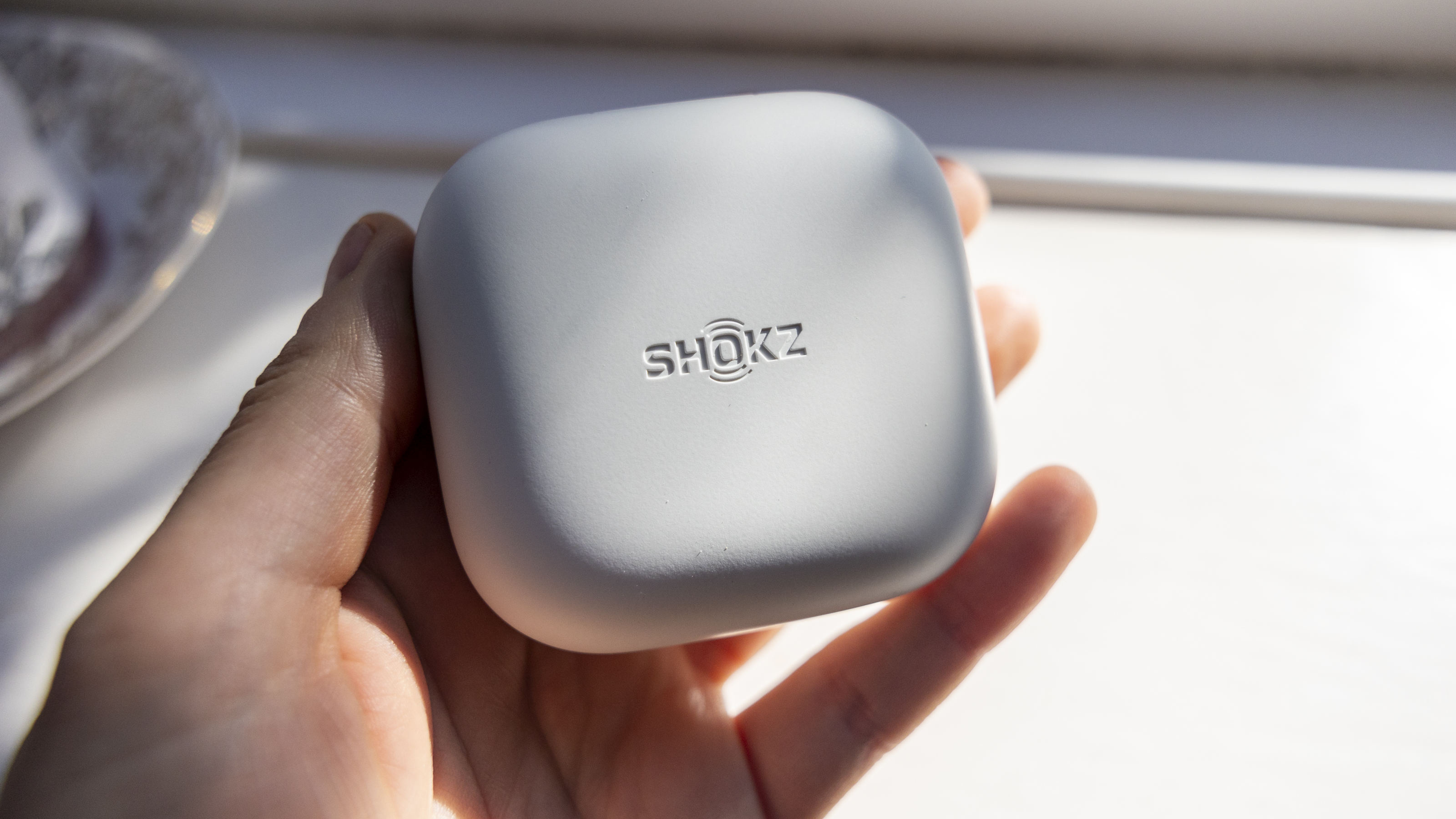 The Shokz OpenFit Air headphone case held in a female hand