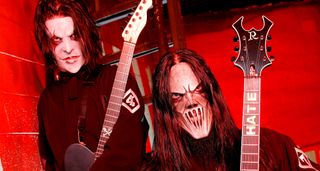 Masked and ready for the stage, Slipknot's Jim Root pose against a red backdrop with their custom Telecaster and B.C. Rich Bich guitars. Thomson's has "HATE" inlaid on frets 2 to 5.