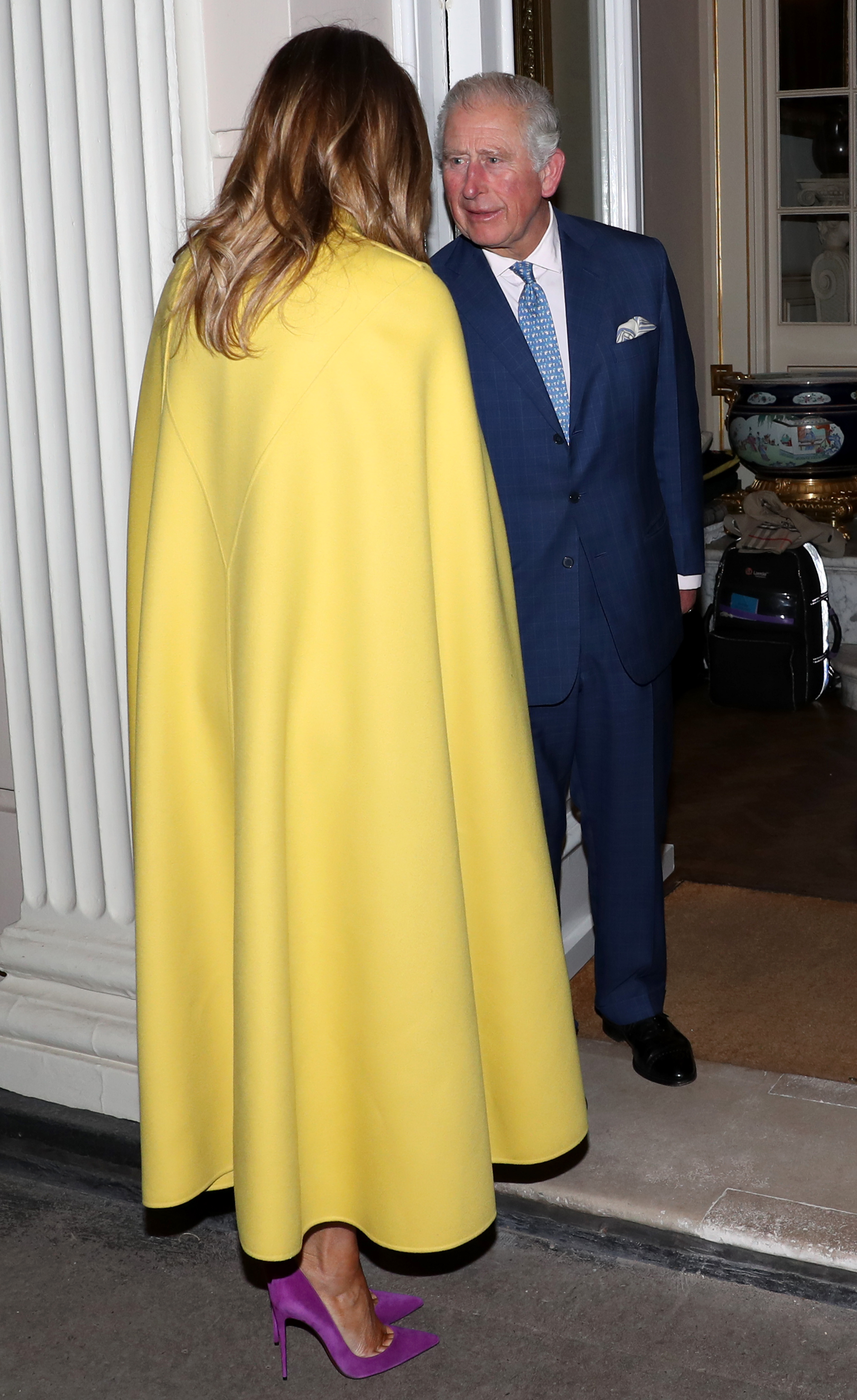 Melania Trump wearing a yellow cape shaking hands with King Charles